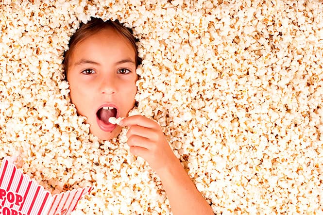 Fille mangeant du pop-corn lors d'une soirée cinéma, entourée de pop-corn.