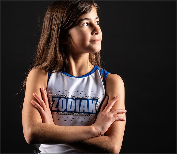 Jeune pom-pom girl en uniforme "Zodiak" avec les bras croisés, prête pour l'entraînement de pom-pom girl.