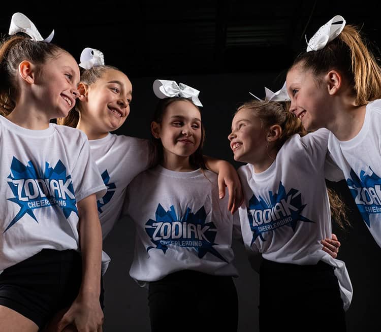 L'équipe de cheerleading Zodiak sourit et se lie d'amitié, portant des chemises blanches et des nœuds.