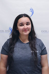 Corinne H. avec un t-shirt gris devant le logo Excel Gym.