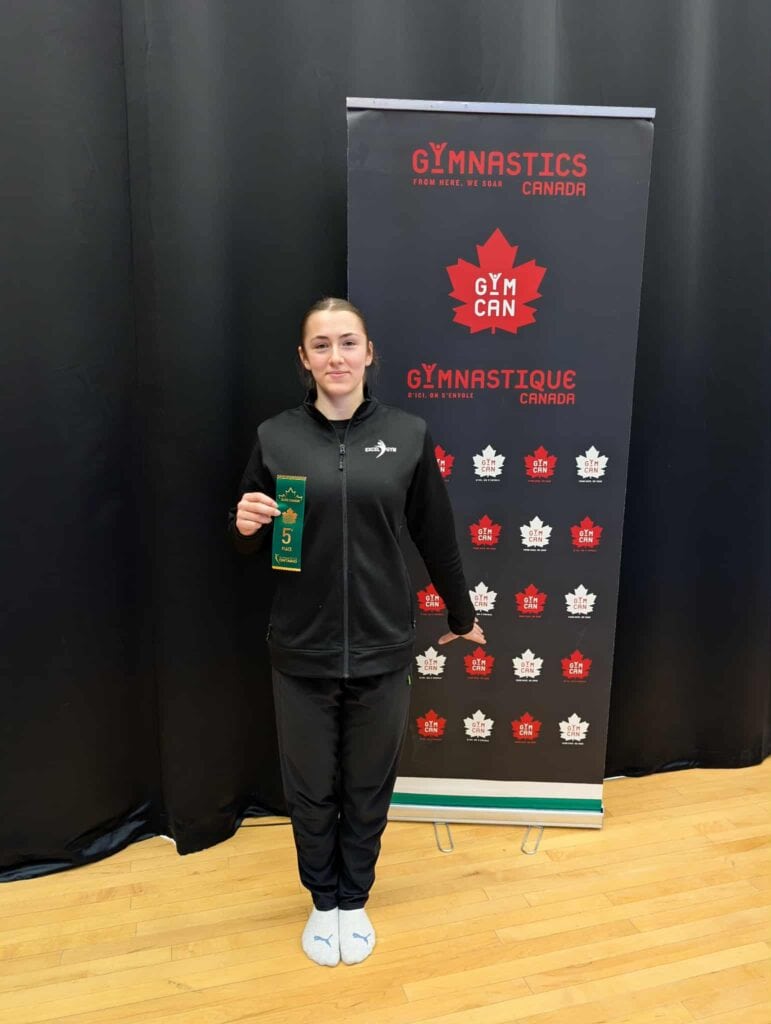 Femme en veste noire avec un badge numéro 5 sur un stand Gymnastics Canada